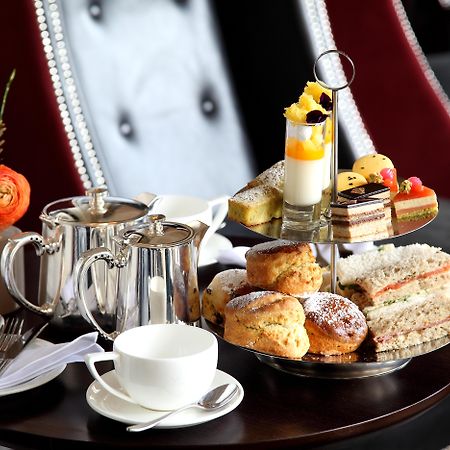 Macdonald Bath Spa Hotel Zewnętrze zdjęcie The photo depicts an elegantly arranged afternoon tea setting. There is a tiered stand filled with a variety of treats, including scones, sandwiches, and small desserts like cakes and pastries. Accompanying this is a teapot and a cup on the table, su
