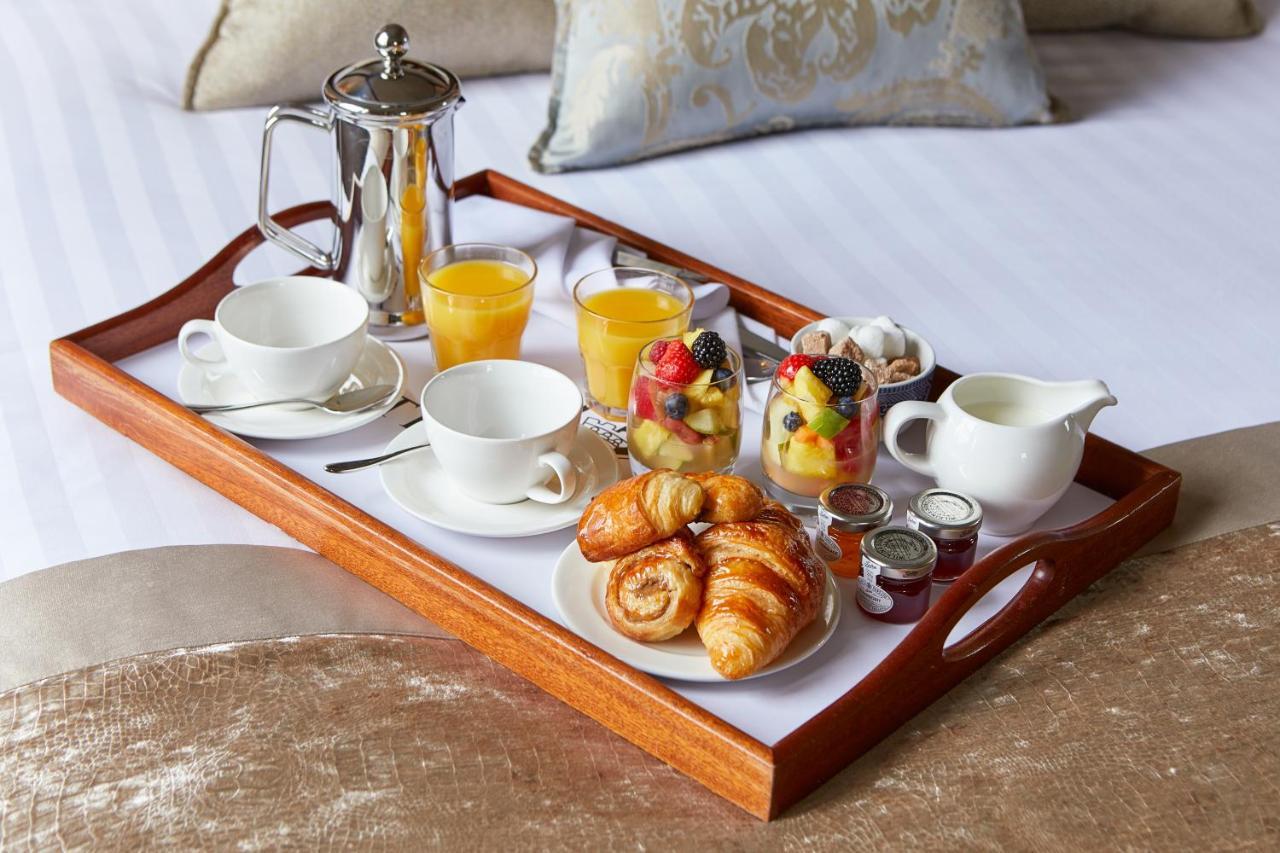 Macdonald Bath Spa Hotel Zewnętrze zdjęcie The photo shows a wooden tray arranged with a delightful breakfast spread. On the tray, there are two cups, a coffee pot, and several glasses of orange juice. There's also a small bowl of mixed fruit, featuring various colorful pieces. Additionally, 