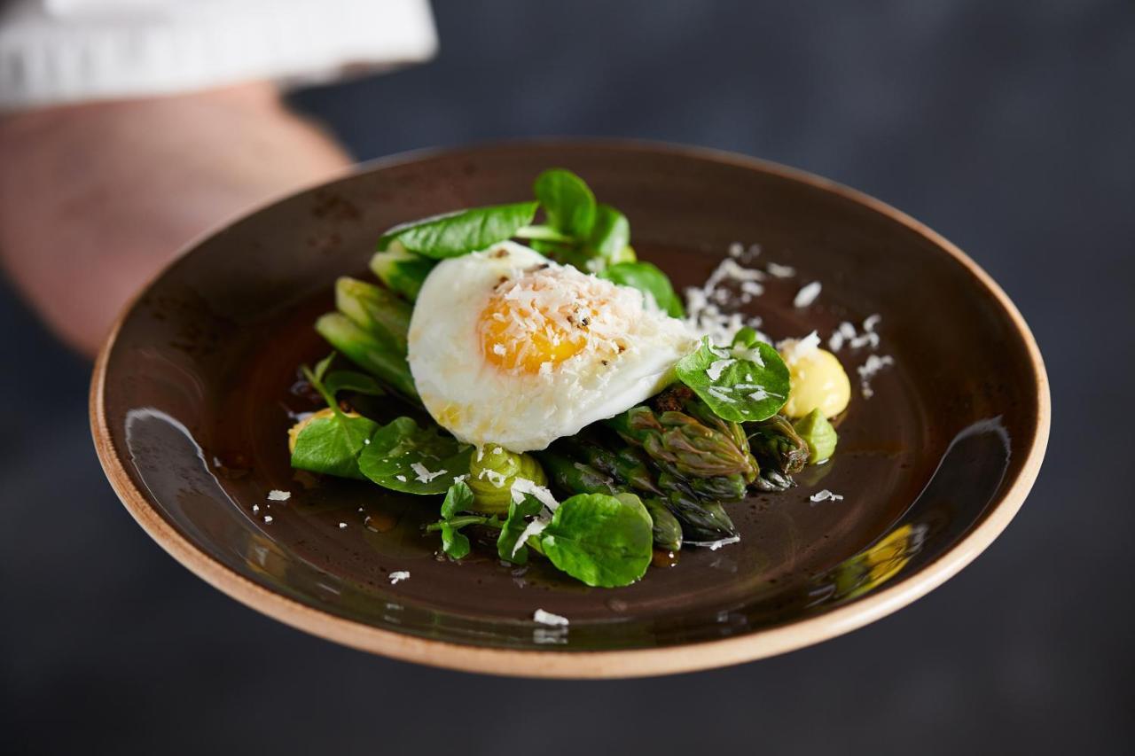 Macdonald Bath Spa Hotel Zewnętrze zdjęcie The photo shows a plate of beautifully arranged food, featuring a poached egg on top of a mix of fresh greens. The greens include asparagus, lettuce, and possibly some herbs, garnished with a sprinkle of grated cheese or a similar topping. The dish i