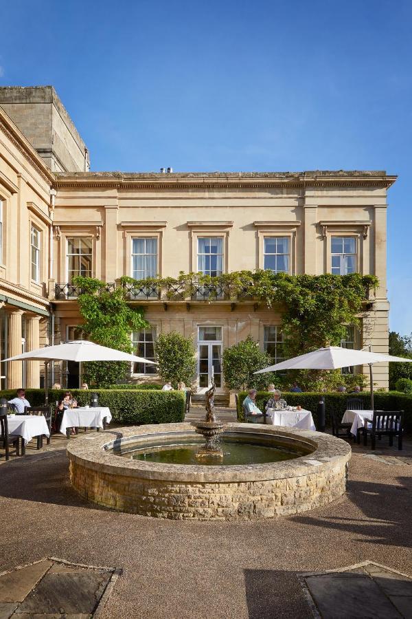 Macdonald Bath Spa Hotel Zewnętrze zdjęcie The photo depicts a charming outdoor dining area of a classic-looking building with elegant architecture. The structure features large windows and is adorned with greenery, including climbing plants. In the foreground, there is a circular fountain, a