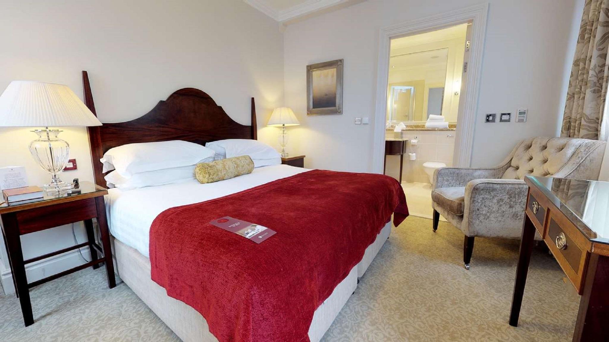 Macdonald Bath Spa Hotel Zewnętrze zdjęcie The photo shows a well-furnished hotel room. In the center, there is a large bed with white linens and a red throw blanket. A decorative pillow is placed on the bed. On either side of the bed, there are bedside tables with lamps. To the right, there 