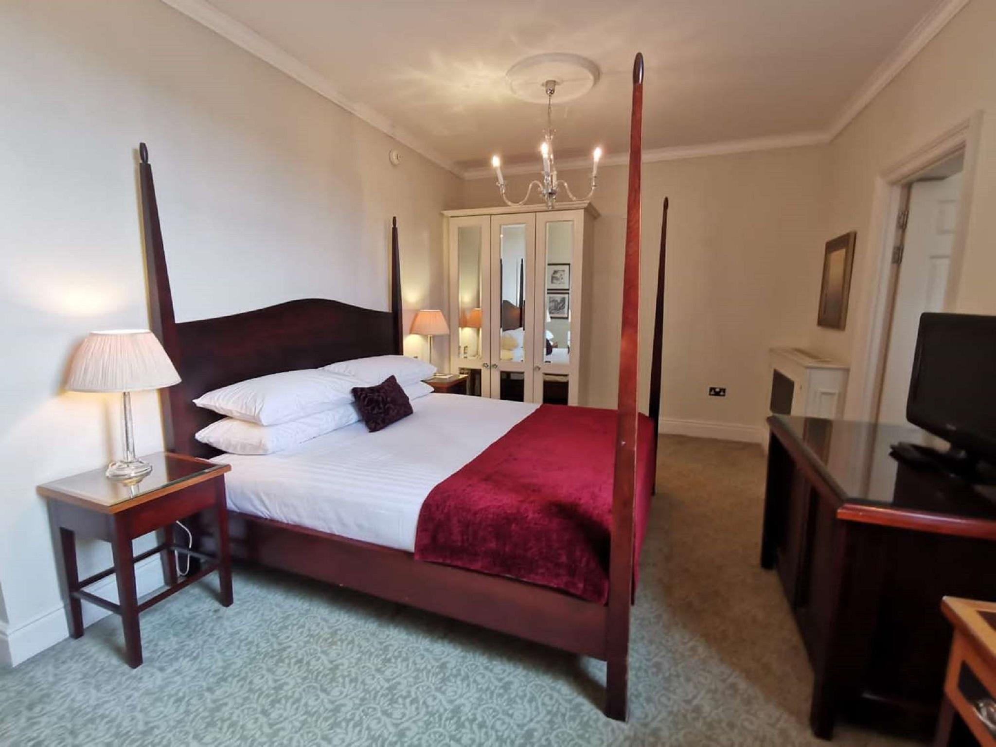 Macdonald Bath Spa Hotel Zewnętrze zdjęcie The photo shows a well-decorated bedroom featuring a four-poster bed with white pillows and a burgundy throw. There are two bedside lamps on wooden nightstands on either side of the bed. A large wardrobe or mirror cabinet is visible in the background