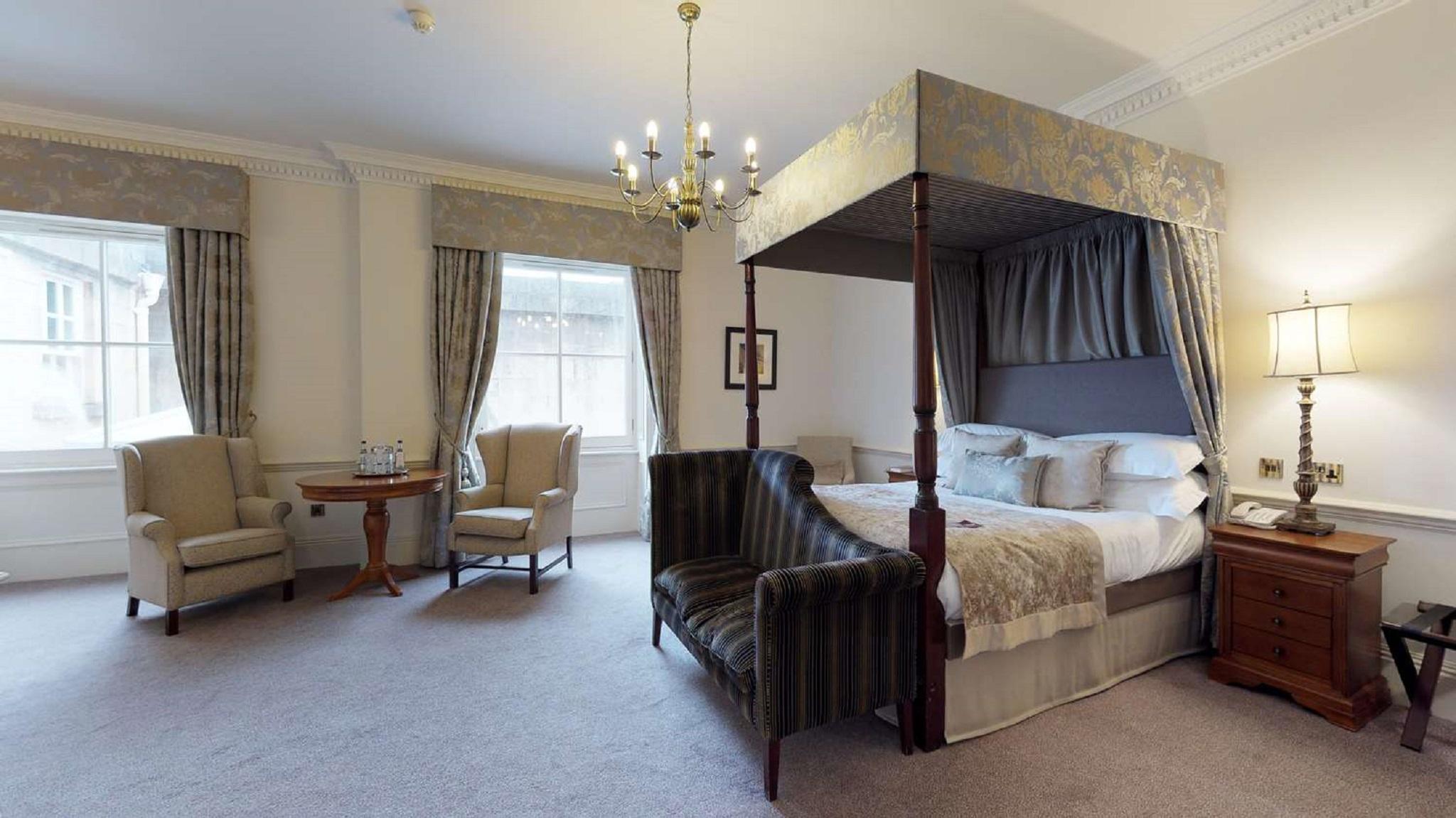 Macdonald Bath Spa Hotel Zewnętrze zdjęcie The photo shows a stylish hotel room featuring a four-poster bed with a decorative canopy. The bed is positioned prominently in the center, surrounded by plush bedding. To the side, there are two armchairs with a small round table between them, creat