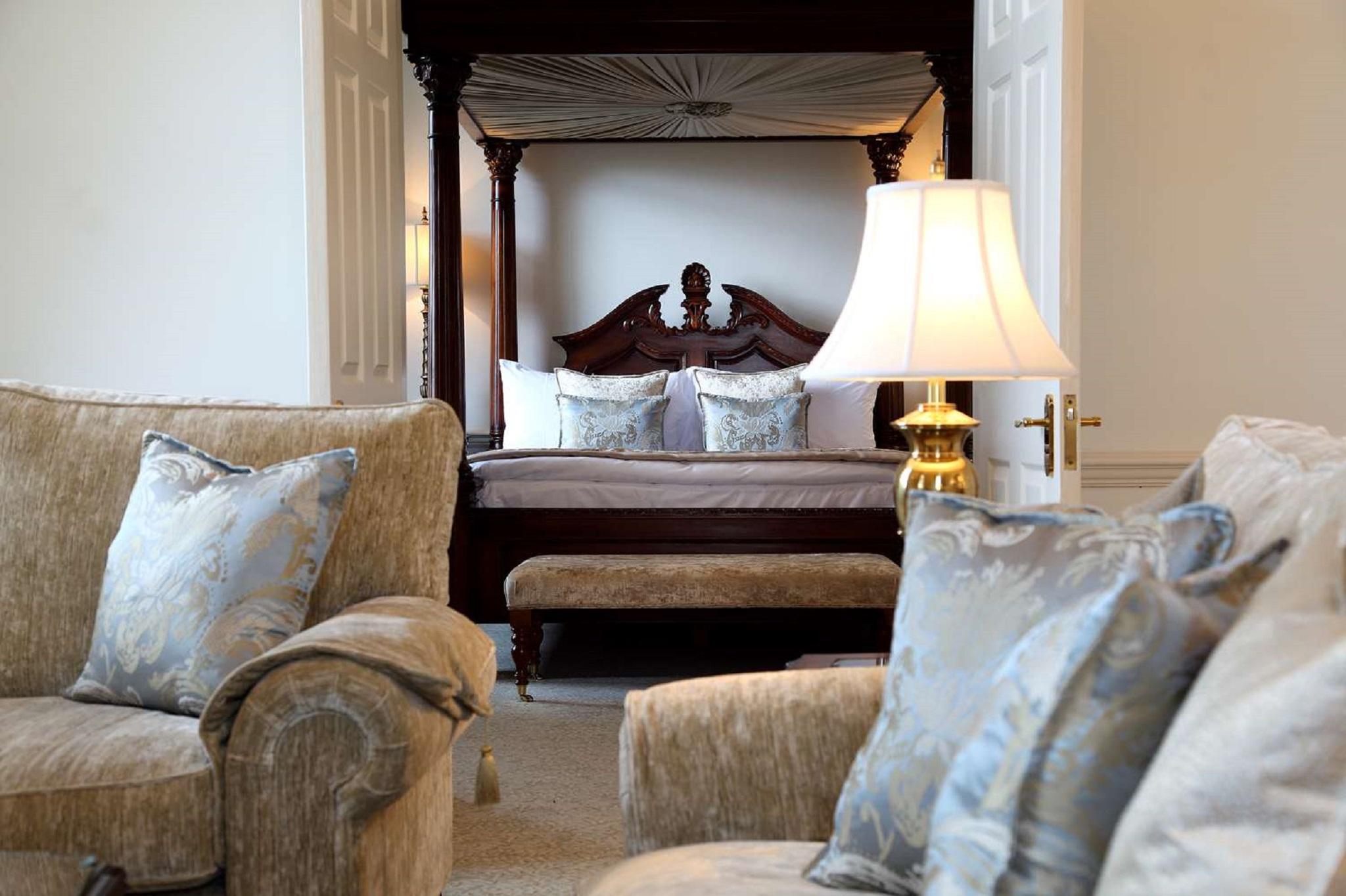 Macdonald Bath Spa Hotel Zewnętrze zdjęcie The photo shows a beautifully decorated room featuring a four-poster bed in the background. The bed has a wooden frame with a rich design, and it is adorned with plush bedding and pillows. In the foreground, there are comfortable sofas with decorativ