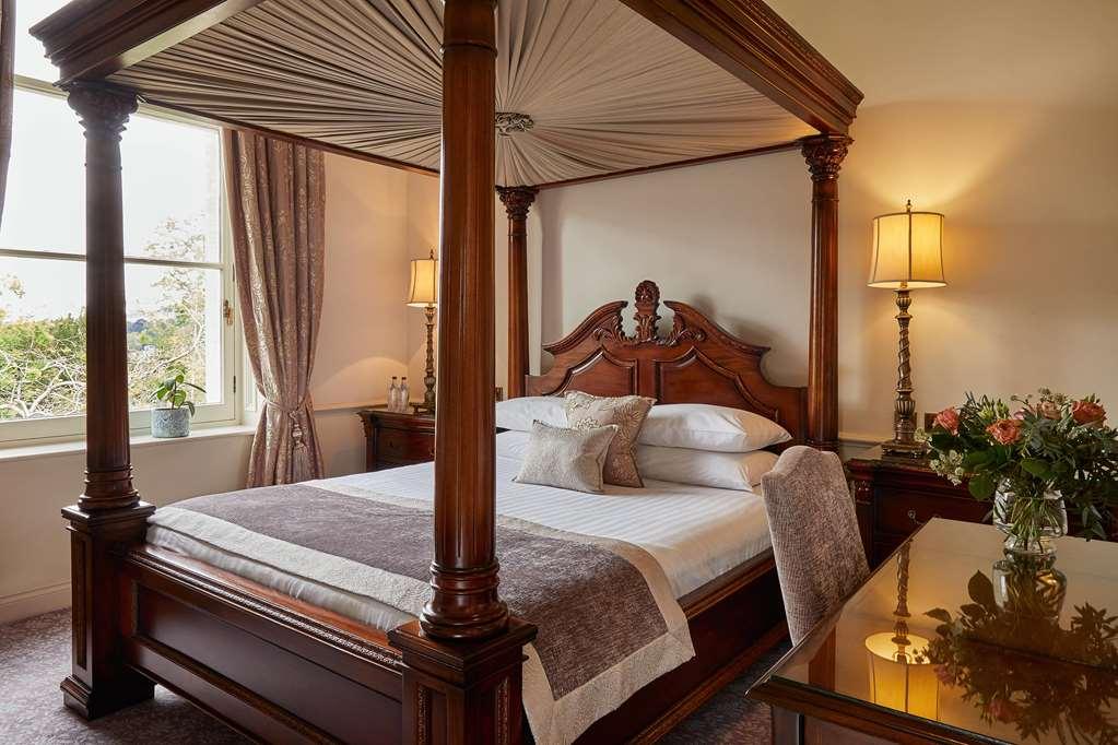 Macdonald Bath Spa Hotel Pokój zdjęcie The photo shows a beautifully designed bedroom featuring a four-poster bed made of dark wood. The bed has an elaborately carved headboard and is adorned with a light-colored bedding set. Above the bed, there is a canopy that adds an elegant touch. On