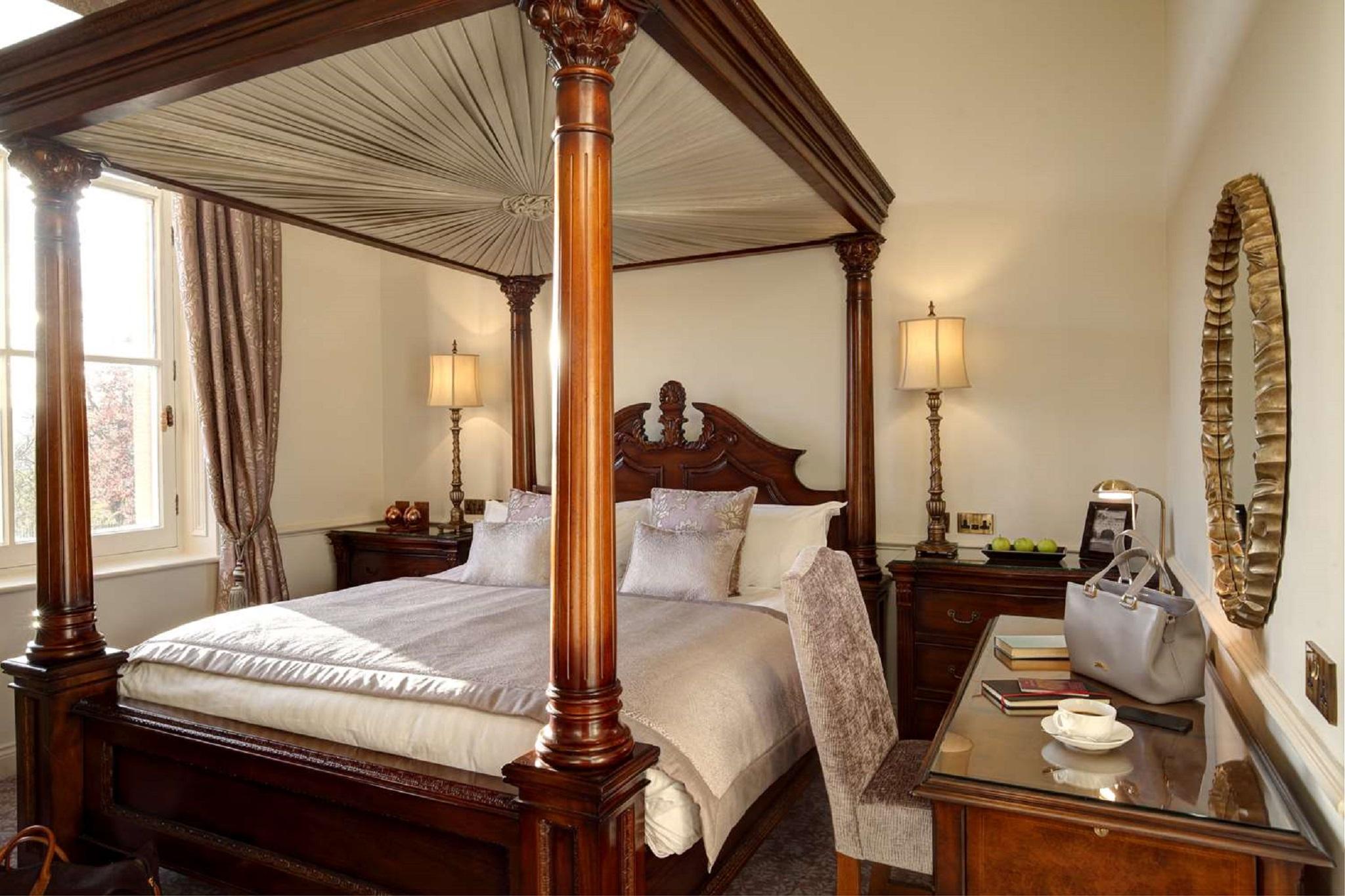 Macdonald Bath Spa Hotel Zewnętrze zdjęcie The photo shows a beautifully designed bedroom featuring a four-poster bed with a canopy. The bed is adorned with white linens and decorative pillows. On either side of the bed, there are bedside tables with lamps providing warm lighting. Large windo