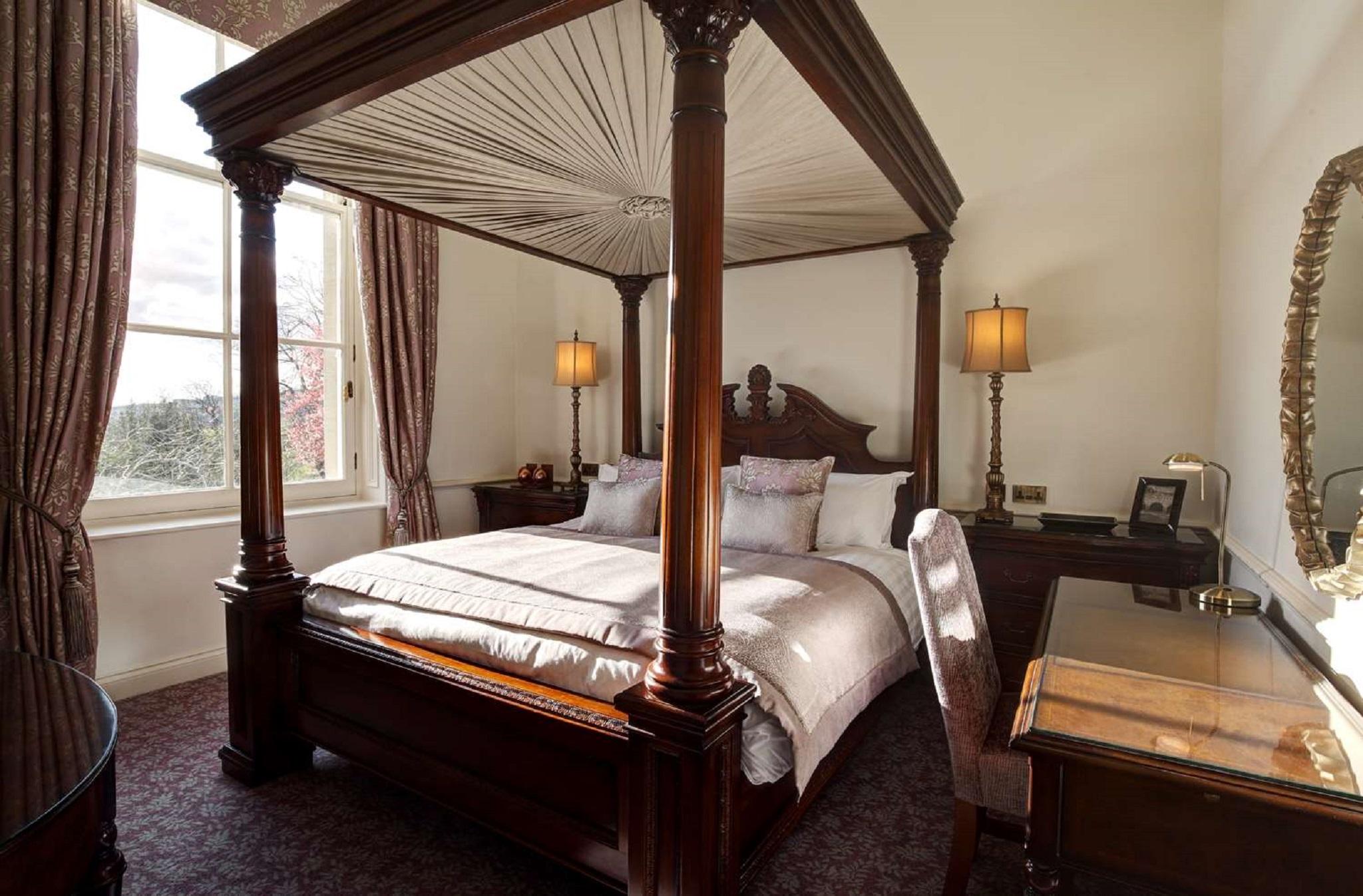 Macdonald Bath Spa Hotel Zewnętrze zdjęcie The photo shows a well-decorated bedroom featuring a four-poster bed with an elegant wooden frame. The bed is dressed with light-colored linens and several decorative pillows. On either side of the bed, there are matching bedside lamps that provide s