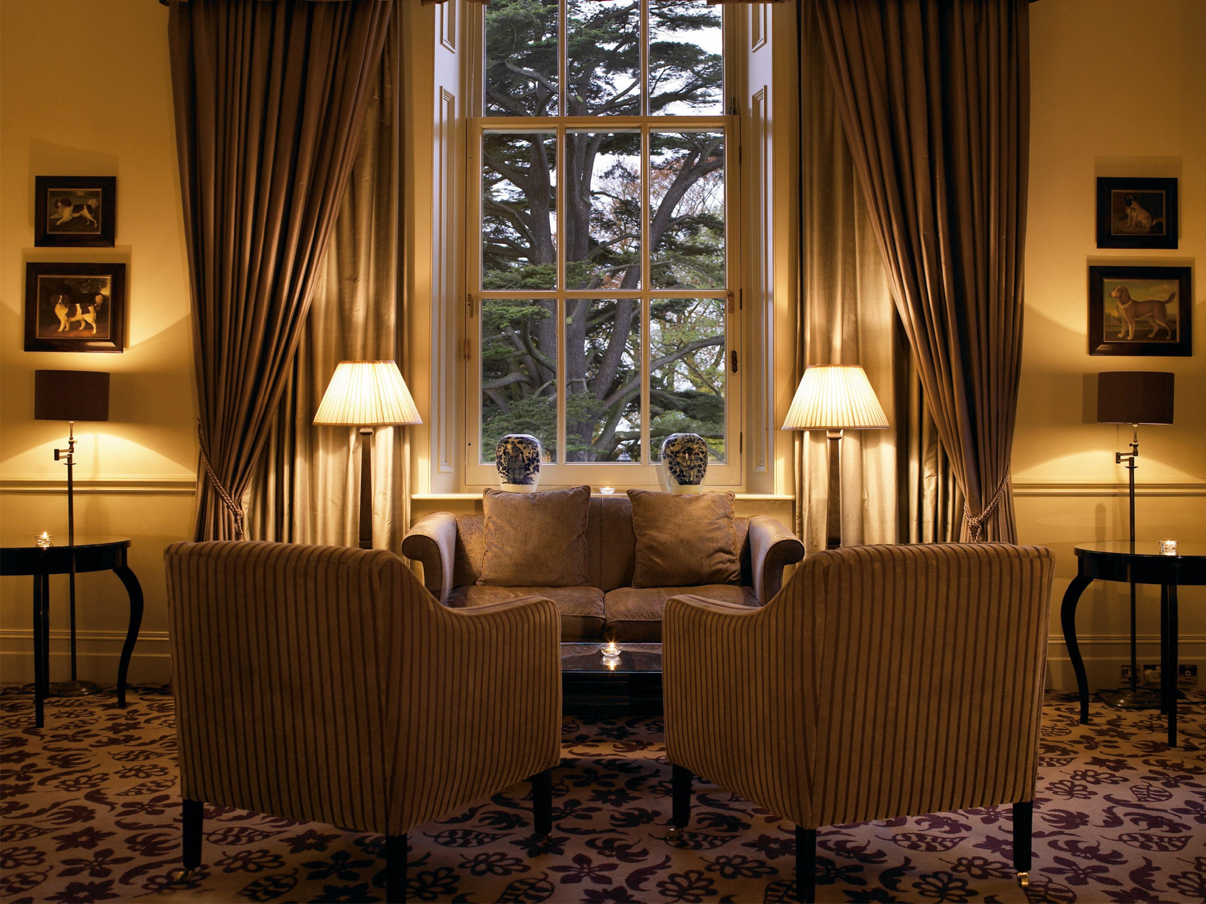 Macdonald Bath Spa Hotel Zewnętrze zdjęcie The photo shows a cozy and elegant sitting area. There are two upholstered armchairs facing a small sofa, all arranged around a central coffee table. Soft lighting is provided by two lamps with white shades, one beside each chair. The window behind t